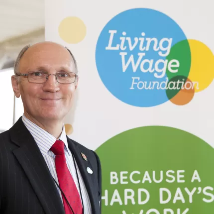 Stuart Wright smiling in front of Living Wage logo