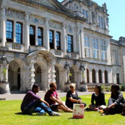 Cardiff University students sitting outside building on the grass