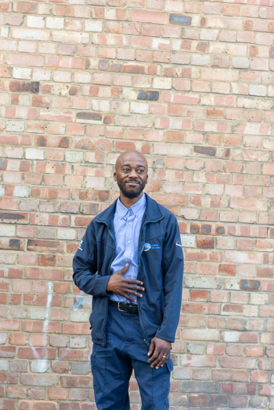 Image of Michael, dressed in a blue Enabled Living workers uniform stood in front of a brick wall