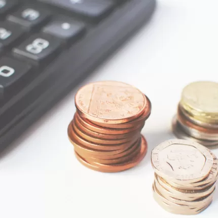 A calculator with three piles of coins next to it