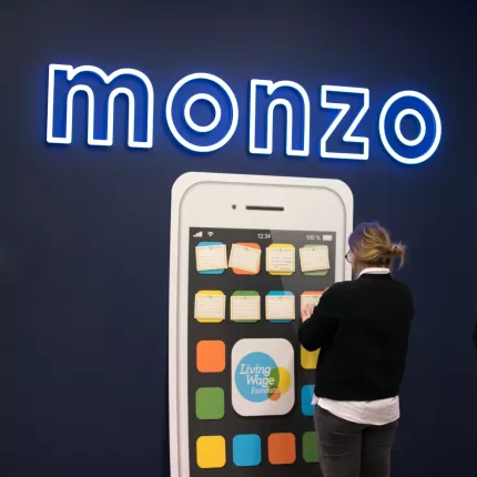 Photo of a monzo and Living Wage Foundation branded wall with a woman standing in front looking at it