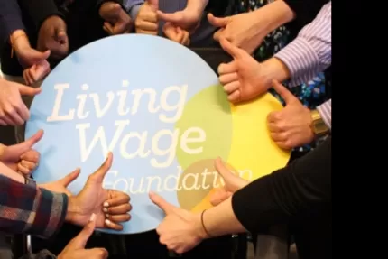 Living Wage Foundation foamboard surrounded by a circle of hands giving it the thumbs up