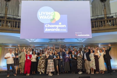 Winners with their hands in the air standing in front of a projector with the Living Wage Champion Awards 2026 logo on it.